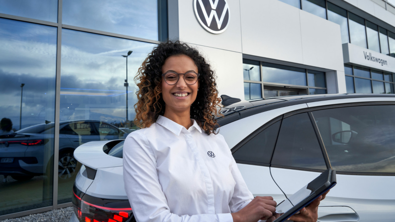Volkswagen servicemedewerker staat buiten met een tablet in haar handen, op de achtergrond een Volkswagen ID.5 en een dealerlocatie