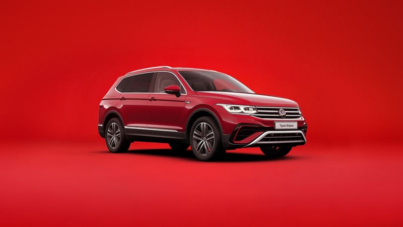Czerwony nowy VW Tiguan Allspace widziany z przodu i z boku na czerwonym tle.