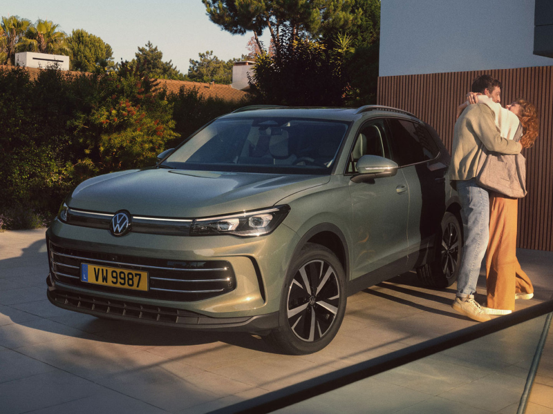 Volkswagen Tiguan Life vert stationné devant une maison moderne, avec deux personnes debout à proximité du véhicule.
