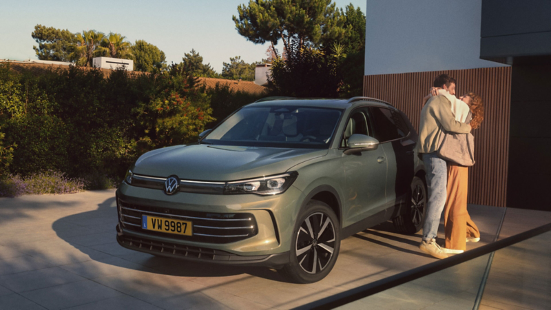 Volkswagen Tiguan Life vert stationné devant une maison moderne, avec deux personnes debout à proximité du véhicule.