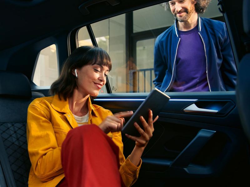 Moteris sėdi ant galinės „VW Tiguan“ sėdynės ir naudoja „We Connect“ per planšetinį kompiuterį