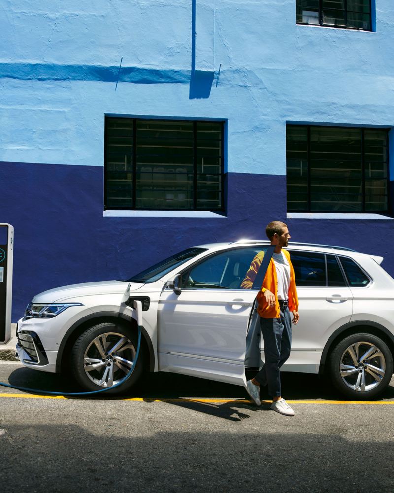 Nouveau Tiguan Hybride Rechargeable blanc en charge en ville devant mur bleu avec homme qui sort de la voiture