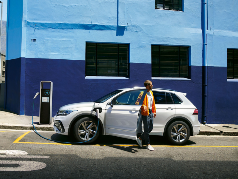 Nouveau Tiguan Hybride Rechargeable blanc en charge en ville devant mur bleu avec homme qui sort de la voiture