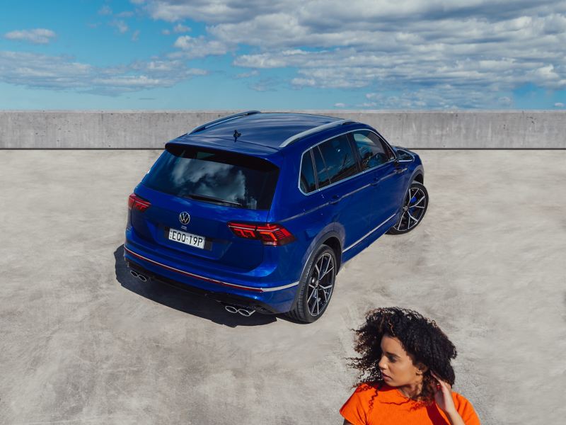 Top angle of the back side view of the Volkswagen Tiguan R with the woman in foreground.