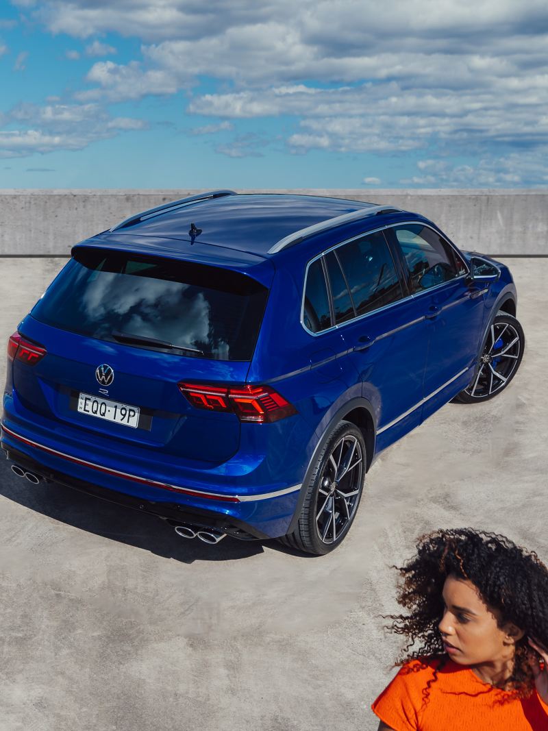 Top angle of the back side view of the Volkswagen Tiguan R with the woman in foreground.