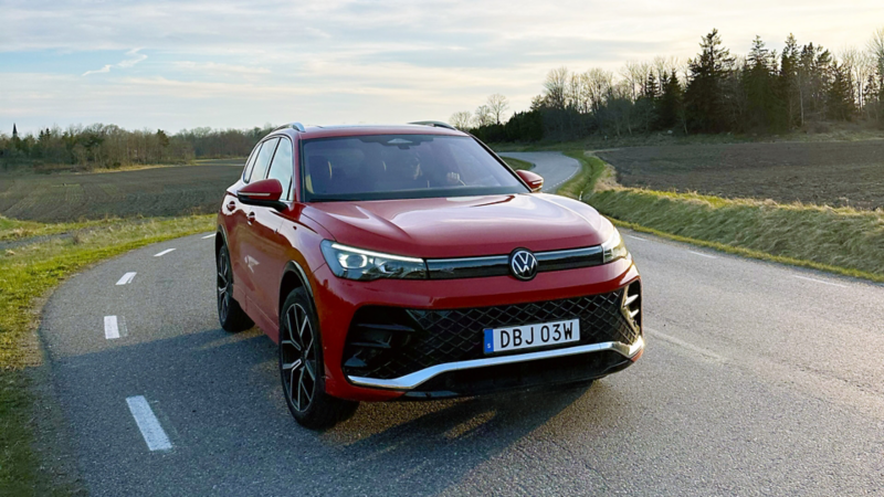 En röd VW Tiguan kör längs en slingrig väg. Skog och åkrar i bakgrunden