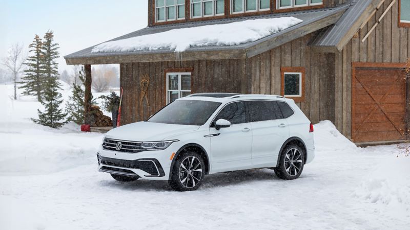The white 2024 Volkswagen Tiguan parked near a wooden house during winter