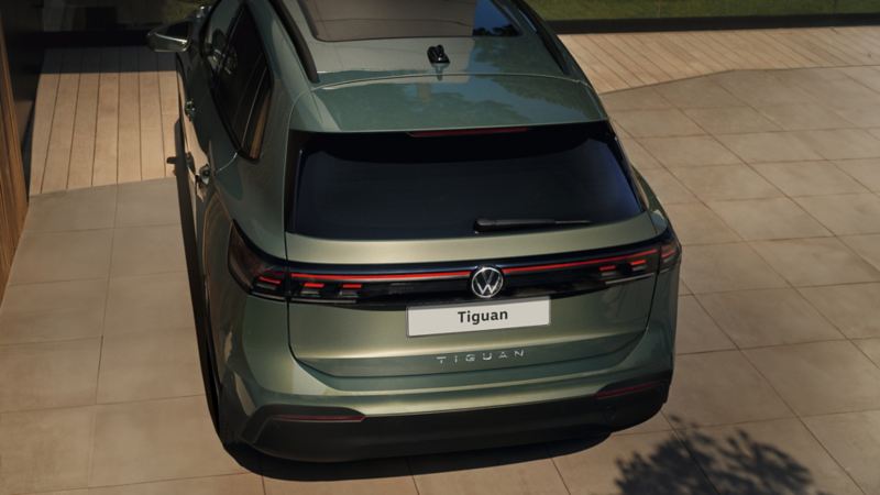 Two VW Tiguan in dark green and red are parked in front of a rocky coastal landscape.