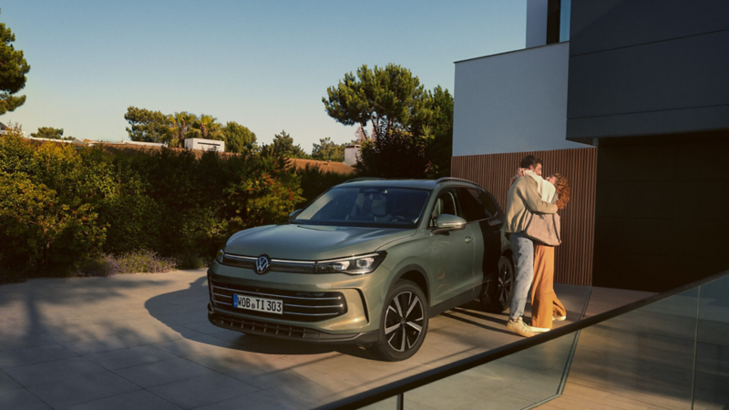 A green Tiguan parked outside a model home as a couple embraces beside it
