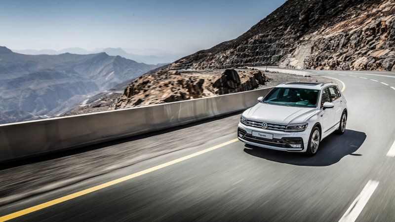 A white Volkswagen Tiguan driving around a mountain bend
