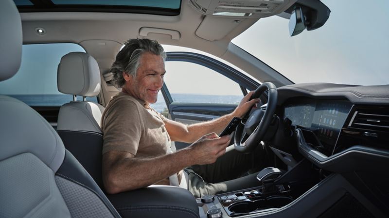 Cilvēks sēž Volkswagen automašīnā ar viedtālruni rokā