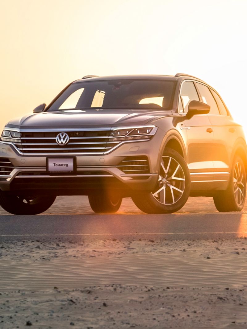 A Volkswagen Touareg parked in the desert with the sun setting behind it