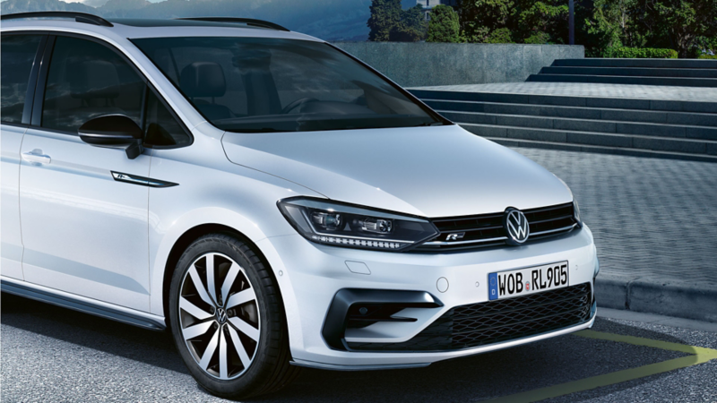 En vit VW Touran R-Line stående vid sidan av vägen. Fokus på motorhuven och den svarta kylargrillen med R-Line-logotyp.