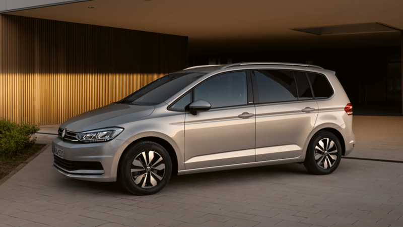 Srebrny Volkswagen Touran stoi zaparkowany na podjeździe eleganckiego domu