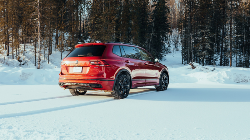 Un Volkswagen Tiguan rouge est montré en train de rouler sur une route enneigée et boisée, soulignant sa capacité de remorquage.