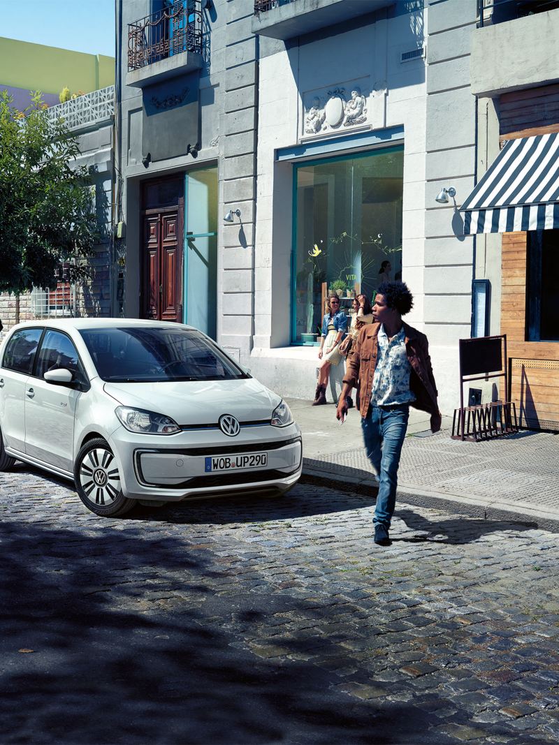 A man with brown coat crossing the road with a white VW in the background