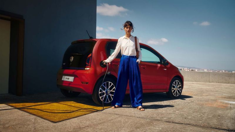 In primo piano una ragazza seduta su un muretto, sullo sfondo una Volkswagen Nuova e-up! vista dall'alto lateralmente.