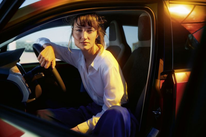   Blick durch die geöffnete Fahrertür ins Innere eines VW e-up!, auf dem Fahrersitzt lehnt eine Frau am Lenkrad, schaut in die Kamera.