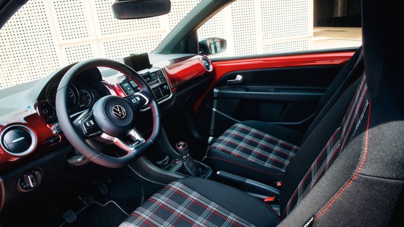 Vue intérieur de la planche de bord de la VW up! GTI et des sièges avec leur sellerie à carreaux rouges, blancs et noirs.