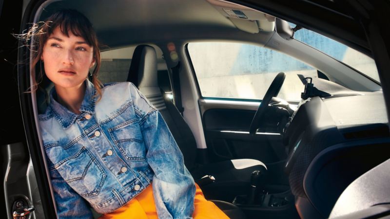 Donna seduta in una Volkswagen up! vista attraverso la portiera del passeggero anteriore nell'abitacolo con cruscotto nero standard