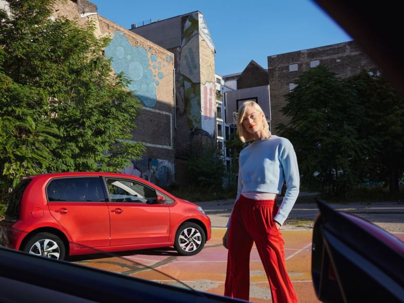Roter VW up! ACTIVE vor grünen Bäumen in Stadt. Blick auf Seite und Räder.