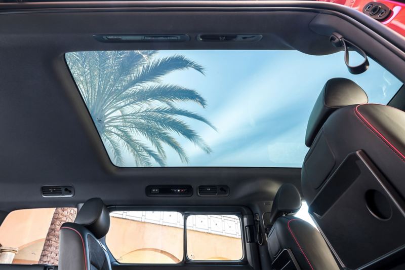 VW ID. Buzz GTX vu intérieure toit transparent sur ciel bleu et palmier, gris et rouge