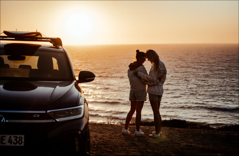 Two women embracing beside a Volkswagen SUV at sunset by the sea.