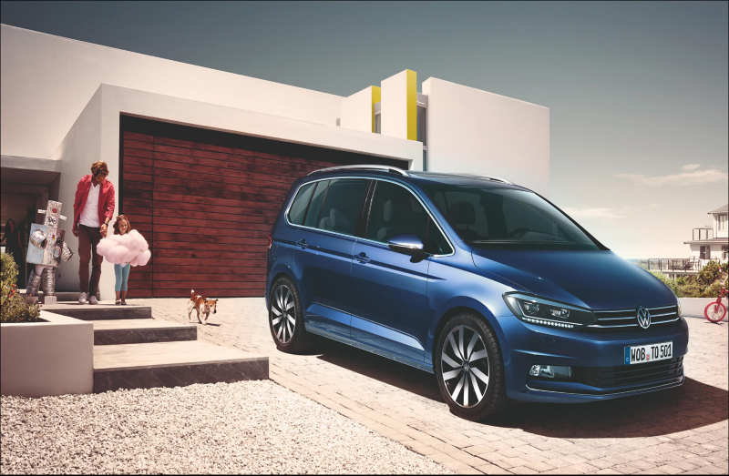 Blue Volkswagen MPV parked outside a modern home with a family nearby