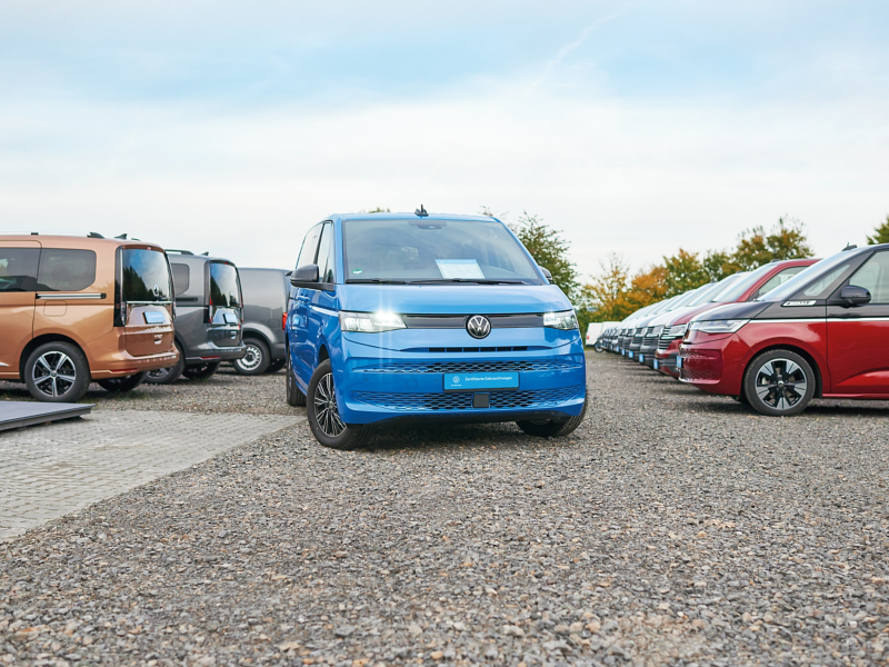 Auf einem Autohof parkende VW Modelle auf Schotter, im Vordergrund steht ein blauer Multivan.