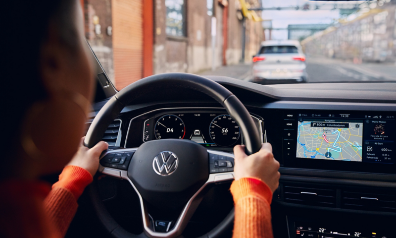 Vue à travers le pare-brise depuis l'intérieur d'une Polo, la conductrice utilisant le contrôle vocal pour activer la navigation.
