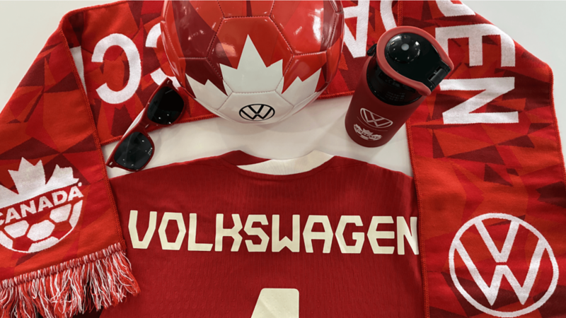 Vue à plat d’articles rouges : écharpe Canada Soccer, ballon VW à feuille d’érable, bouteille, lunettes et chandail « VOLKSWAGEN ».