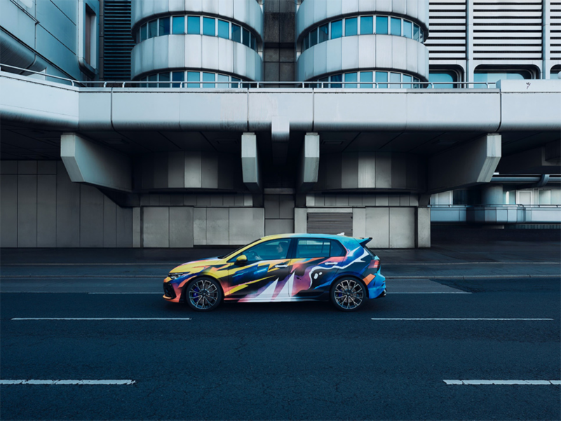 Ein bunter Volkswagen Golf R fährt vor einem futuristischem Gebäude auf der Straße.