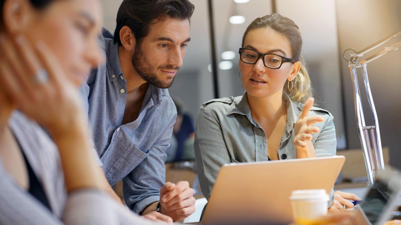 A young woman and a young man are having a conversation while looking at a laptop screen