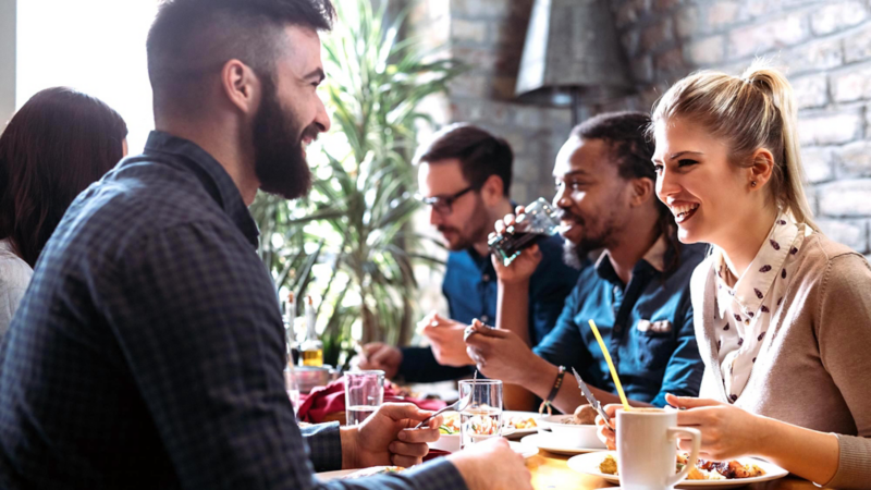 A group of five young people are sitting at a table with food and drinks, chatting