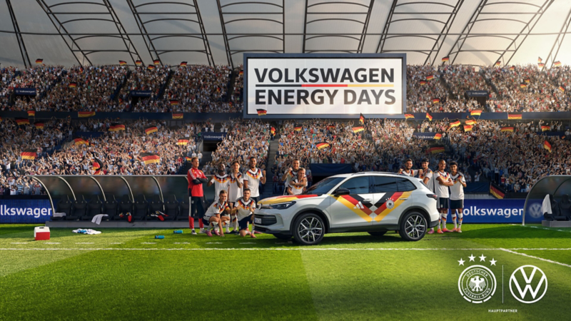 Ein Volkswagen Tiguan im Design des Trikots der Fußballnationalmannschaft steht mit der Herrennationalmannschaft auf dem Rasen eines Stadions. 