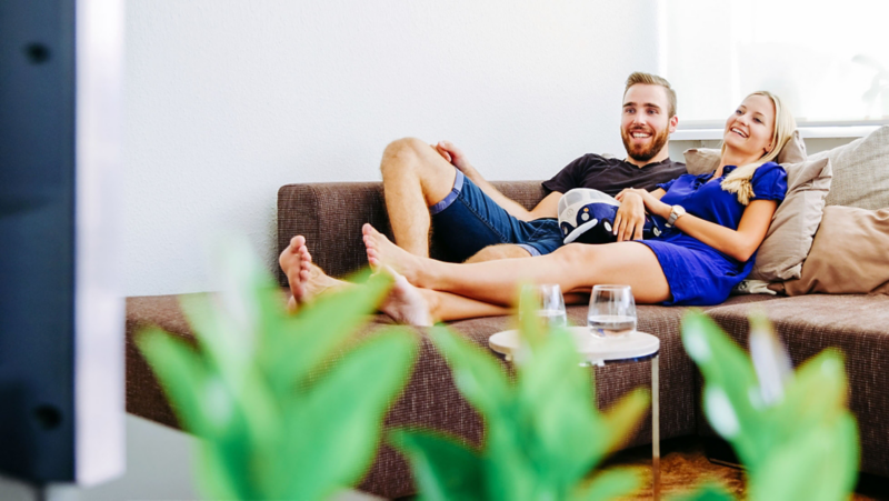 Mann und Frau liegen auf einem Sofa und schauen TV