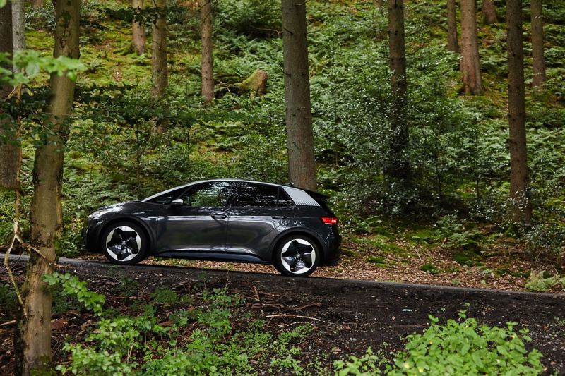 Ein VW ID.3 Elektroauto fährt an einem Waldstück eine steile Straße hoch.