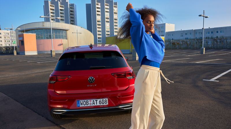 Rear view of the red VW Golf ACTIVE. A woman stands in front of it.