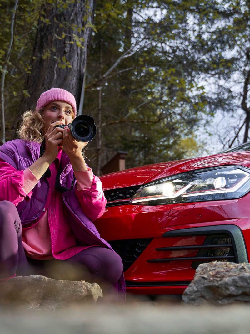 Una donna intenta a fotografare il paesaggio a fianco di una vettura Volkswagen 
