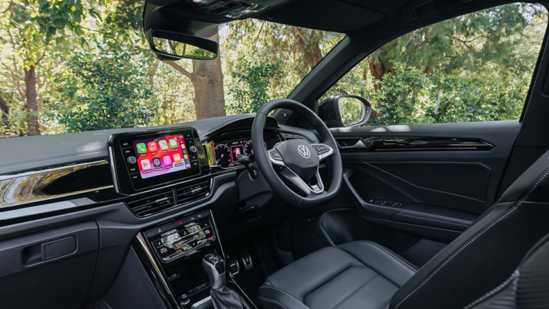 Top angle of the woman holding steering wheel of the Volkswagen T-Roc with open sunroof.