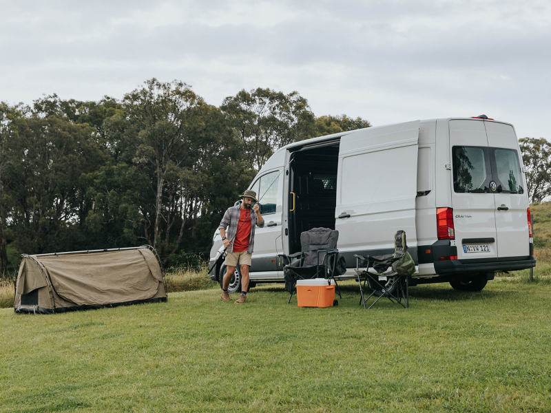 Man with a camping set up holding a fishing pole in front of open Crafter Van