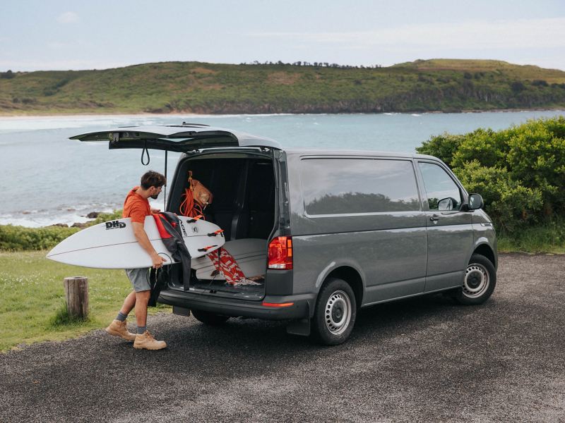 Man placing his surf board from boot door of the Volkswagen Transporter.