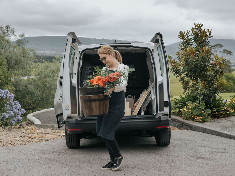 Women with flower pot and tools in the back of the Volkswagen Caddy Cargo.