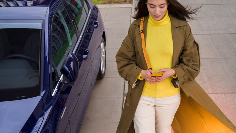 Kvinna med mobiltelefon bredvid bil