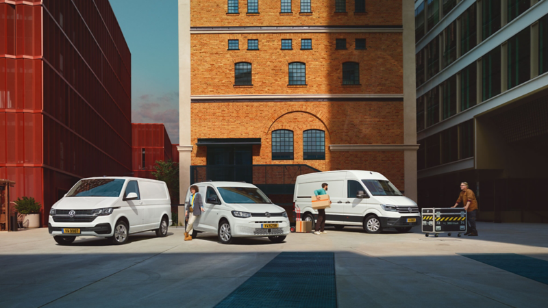  Trois fourgonnettes Volkswagen blanches sont garées devant des bâtiments, avec des personnes chargeant des objets.