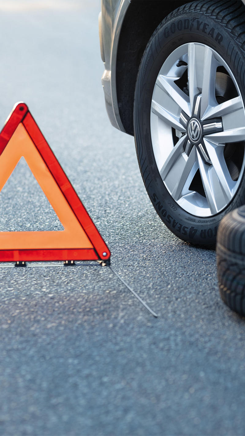  Un triangle de signalisation orange est posé sur l'asphalte près de la roue d'une voiture et d'un pneu de rechange.