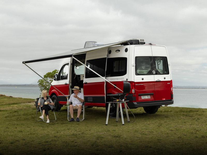 Couple sat outside red and white kampervan 