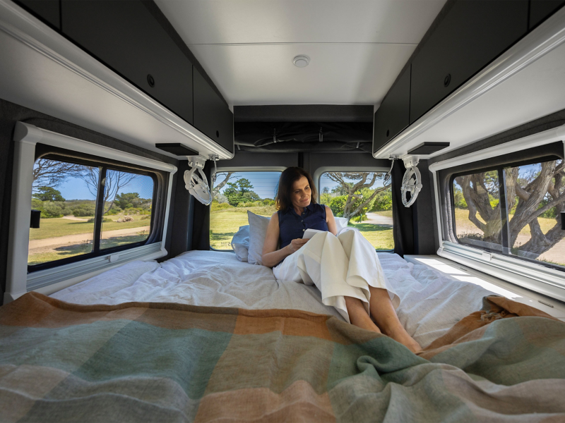 Woman sat in Kampervan sleeping area reading book