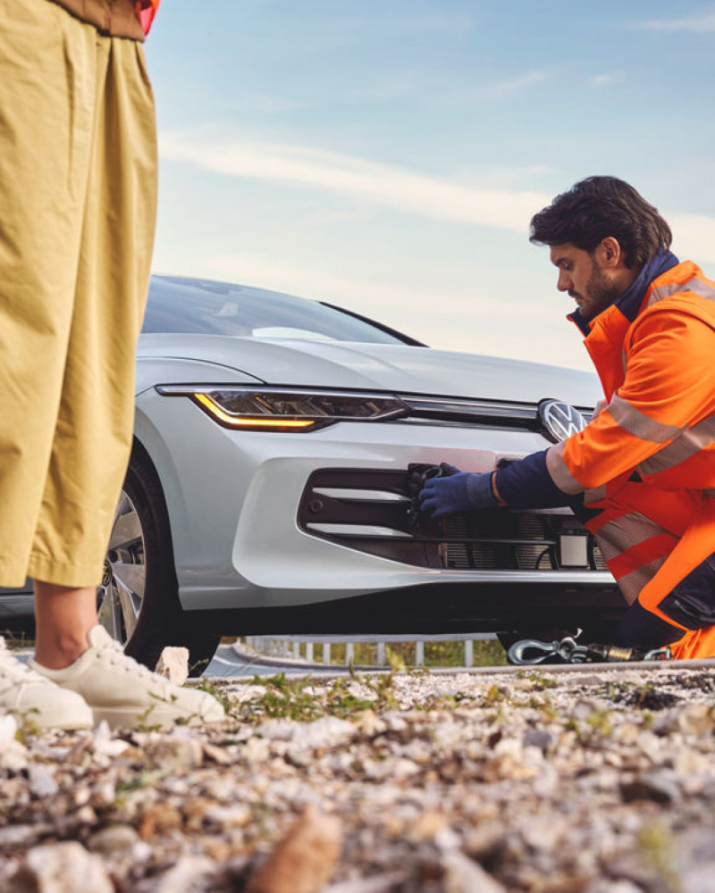 A roadside assistant in an orange overall helps a VW vehicle, symbolizing outdoor adventures.