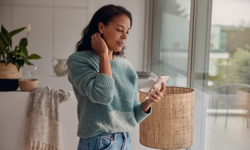 Une femme consulte son smartphone dans son salon.